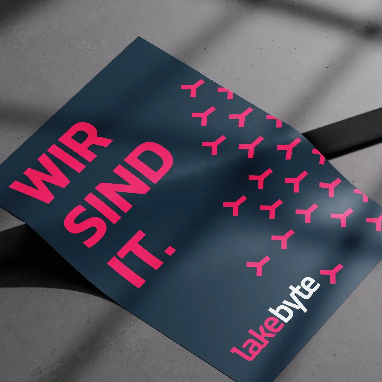Lakebyte-Plakat mit dem Statement ‚WIR SIND IT.‘ auf dunkelblauem Hintergrund mit markantem Muster.